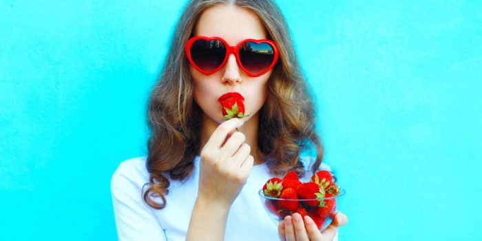 Portrait pretty woman with many strawberry over colorful blue
